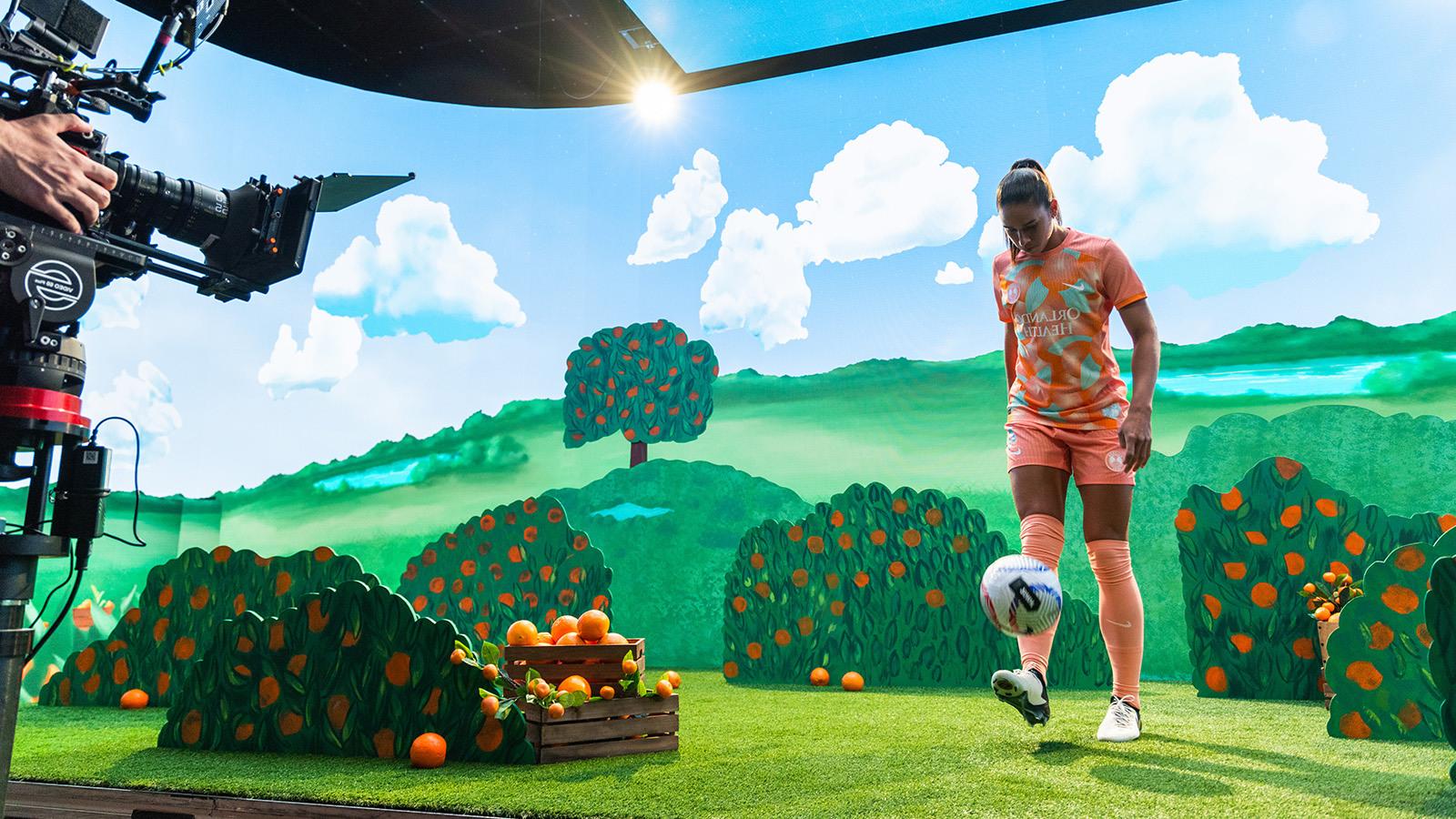一名奥兰多骄傲队的球员将足球踢向电影拍摄现场的摄像机，画面上是一片橘子树林.