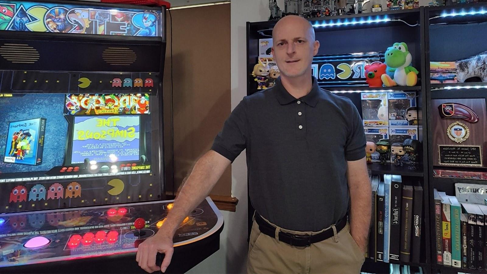 Jason Hutchins standing next to an arcade machine while wearing a blue polo and tan slacks.