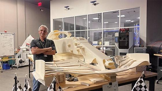 Course Director Pat Starace, a man with white hair and a grey polo shirt, standing next to a large workbench with a 3D-printed replica of a Formula 1 race car in Full Sail’s SimLab.