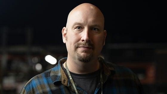 Headshot of Andrew Garraway wearing a blue and grey plaid flannel and a 满帆 lanyard, 配有全帆别针.