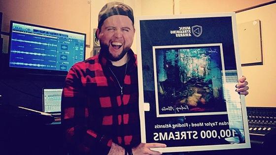 Jordan Moed stands in his studio and holds an award for 10,他的歌曲《寻找亚特兰蒂斯》的播放量达到了5000次.”