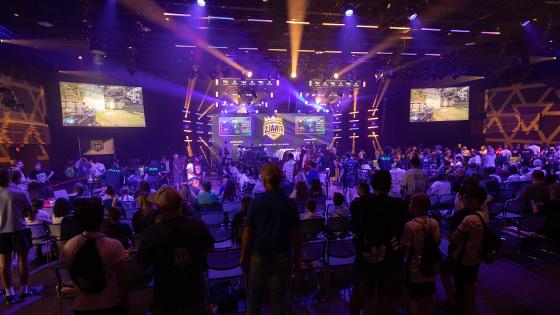 A large crowd in a venue spectating an esports match, 房间前面的一个大LED屏幕上写着“北美总决赛”.’