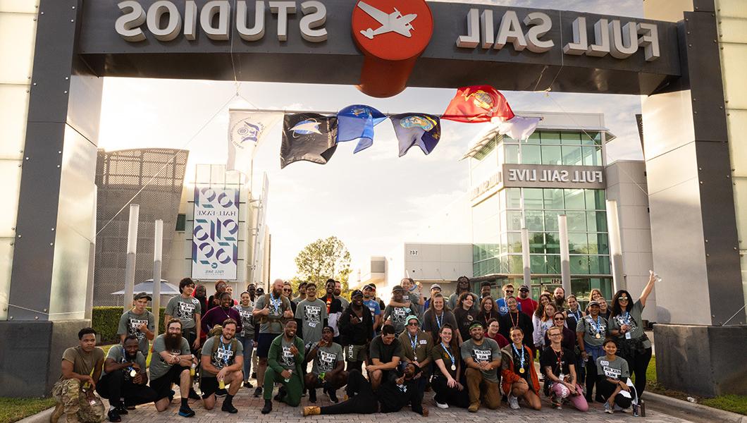 Dozens of student veterans gather under the Full Sail Studios sign in front of the Full Sail Live venue at sunset.